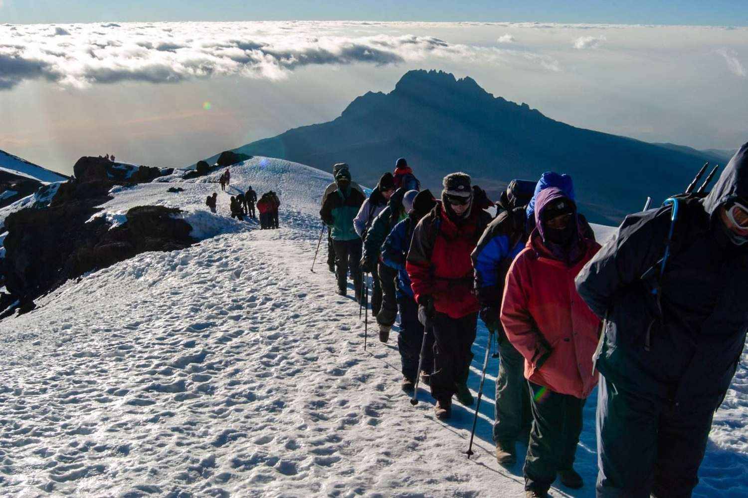 Line of climbers on the snowy Kilimanjaro ridge above the clouds